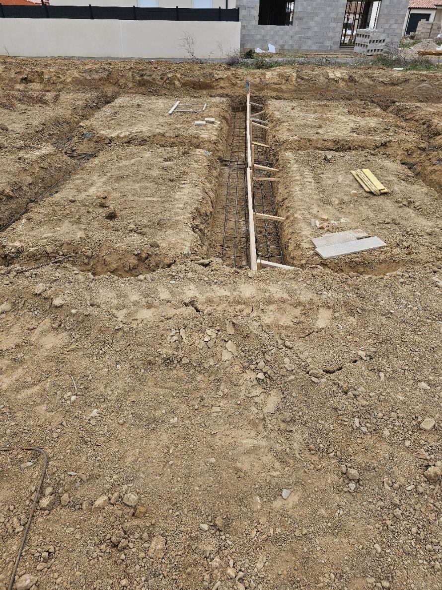 Fouilles ouvertes dans la terre et semelles de fondation ferraillées, avant coulage du béton, sur un chantier de maison neuve
