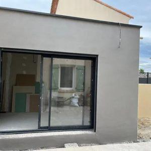 Extension maçonnée enduite, équipée d'une grande baie vitrée coulissante, sur une maison individuelle