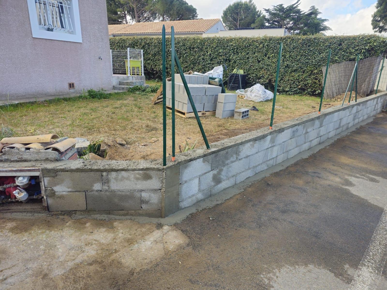 Mur de clôture avec poteaux verts scellés dans le béton avant pose du grillage souple à Vinassan