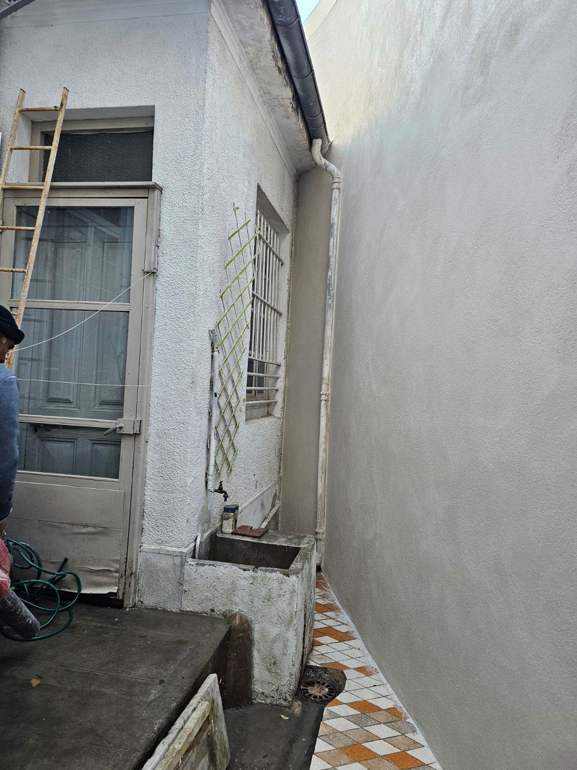 Courette d'une maison pendant un ravalement : le mur de droite vient de recevoir son enduit, l'ancien crépi de la façade de gauche est encore visible